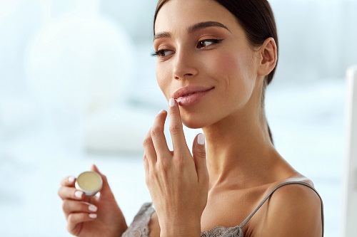 a woman applying lip balm to lips enhanced with lip fillers.