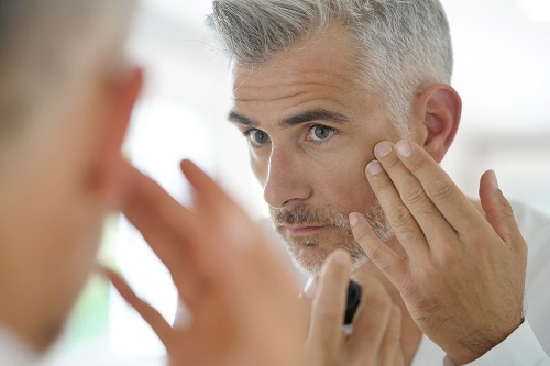 Man in the mirror considering cosmetic treatment for men.