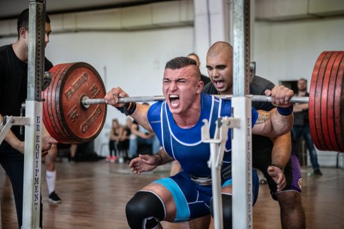 Man doing power lifting assisted by trainer.