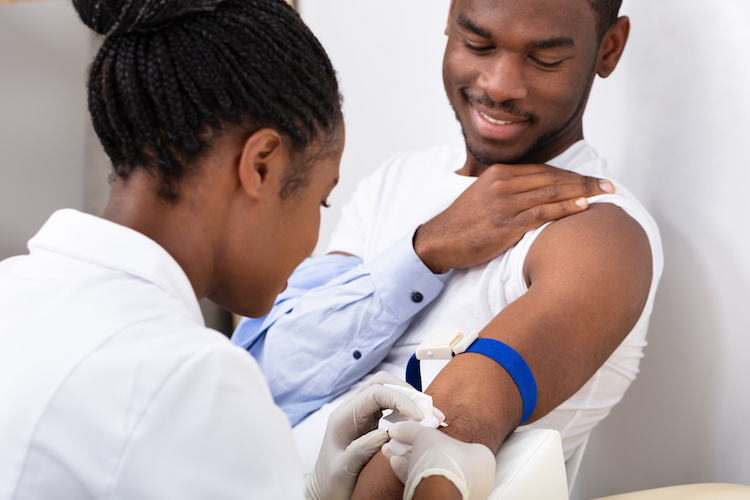 Female Doctor Injecting Male Patient With Syringe To Collect Blood Sample