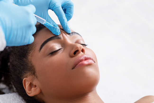 Young african woman receiving botox injection in interbrow zone 