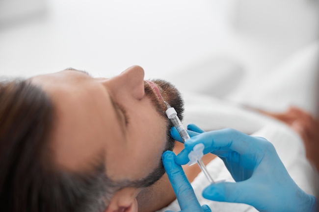 Handsome man undergoes lip augmentation with professional beautician doing filler injection in clinic