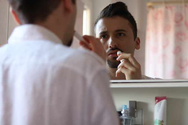 Man Applying Lip Balm while Looking in the Mirror.