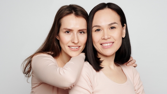 Portrait of positive attractive multi-ethnic girls embracing against white background