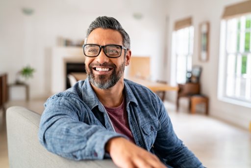 Happy mature middle eastern man wearing eyeglasses sitting on couch.