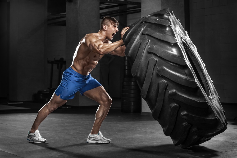 Muscular man working out in gym flipping tire