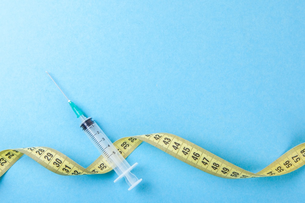 Syringe with a needle and yellow measuring tape