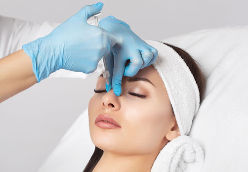 A professional applying a cosmetic treatment with a syringe to a patient's forehead during a skincare procedure.